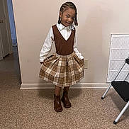 Arianna is registered to the contest to win money with this photo: child, girl, indoor, standing, brown_boots, plaid_skirt, brown_vest, white_shirt, smile, pose, floor, wall, step_ladder, doorway, braided_hair, fashion, clothing, happy, person, portrait