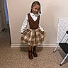 child, girl, indoor, standing, brown_boots, plaid_skirt, brown_vest, white_shirt, smile, pose, floor, wall, step_ladder, doorway, braided_hair, fashion, clothing, happy, person, portrait