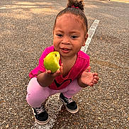 Sorayya joined the competition — help win amazing prizes! child, toddler, apple, bite, pink_clothing, hair_bun, sneakers, asphalt, parking_lot, cars, houses, outdoor, daylight, playful, happy, crouching, holding, food, smiling, person