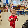 chairs, child, classroom, curtains, education, floor, happy, indoor, person, playroom, preschool, red_clothing, running, shelves, smiling, tables, toddler, toys, windows, young_children