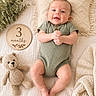 Ryland joined the competition — help win amazing prizes! baby, infant, smiling, green_romper, crocheted_teddy_bear, wooden_sign, 3_months, blanket, pillow, soft_texture, cozy, lying_down, cute, child, happy, indoor, portrait, baby_pose, knitted, warm_colors
