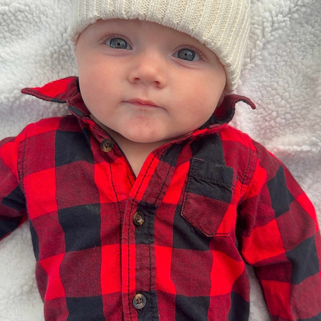 Waylon joined the competition — help win amazing prizes! baby, blanket, blue_eyes, buttoned_shirt, casual_wear, checkered_shirt, child, cozy, cute, face, hat, infant, knit_hat, lying_down, plaid, pom_pom, portrait, red_shirt, soft_texture, warm_clothing