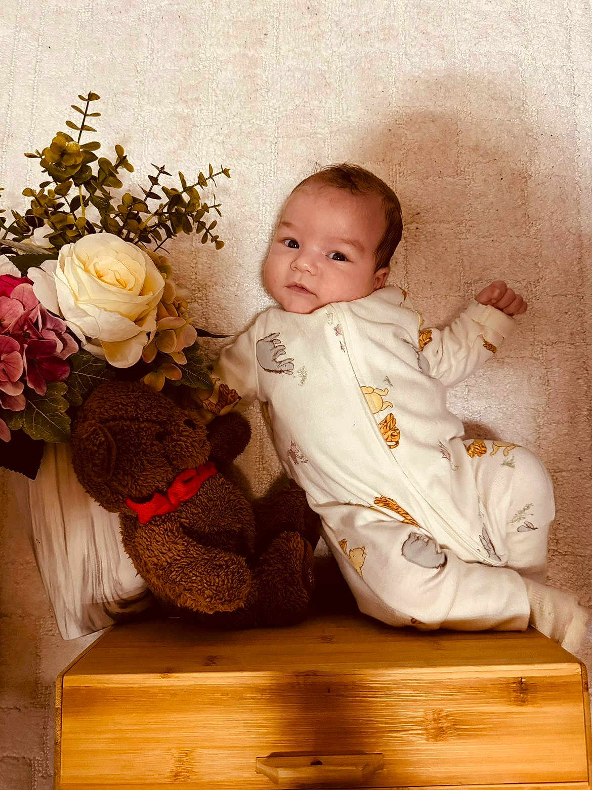 Kenny a rejoint le concours — aidez-le/la à gagner de superbes lots ! baby, infant, toddler, face, smile, teddy_bear, stuffed_toy, flowers, rose, bouquet, plant, foliage, onesie, blanket, wooden_box, furniture, portrait, cozy, shadow, plush