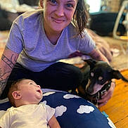 Micah is registered to the contest to win money with this photo: animal, baby, casual_clothing, child, cloud_pattern, curious, cushion, dog, family, happy, home, indoor, person, pet, portrait, relaxed, smiling, tattoo, woman, wood_floor