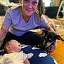 animal, baby, casual_clothing, child, cloud_pattern, curious, cushion, dog, family, happy, home, indoor, person, pet, portrait, relaxed, smiling, tattoo, woman, wood_floor