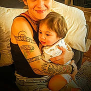 Micah joined the competition — help win amazing prizes! adult, baby, tattoo, hug, couch, home, people, smile, jeans, sitting, casual, indoor, comfort, child, affection, person, portrait, warmth, love, family