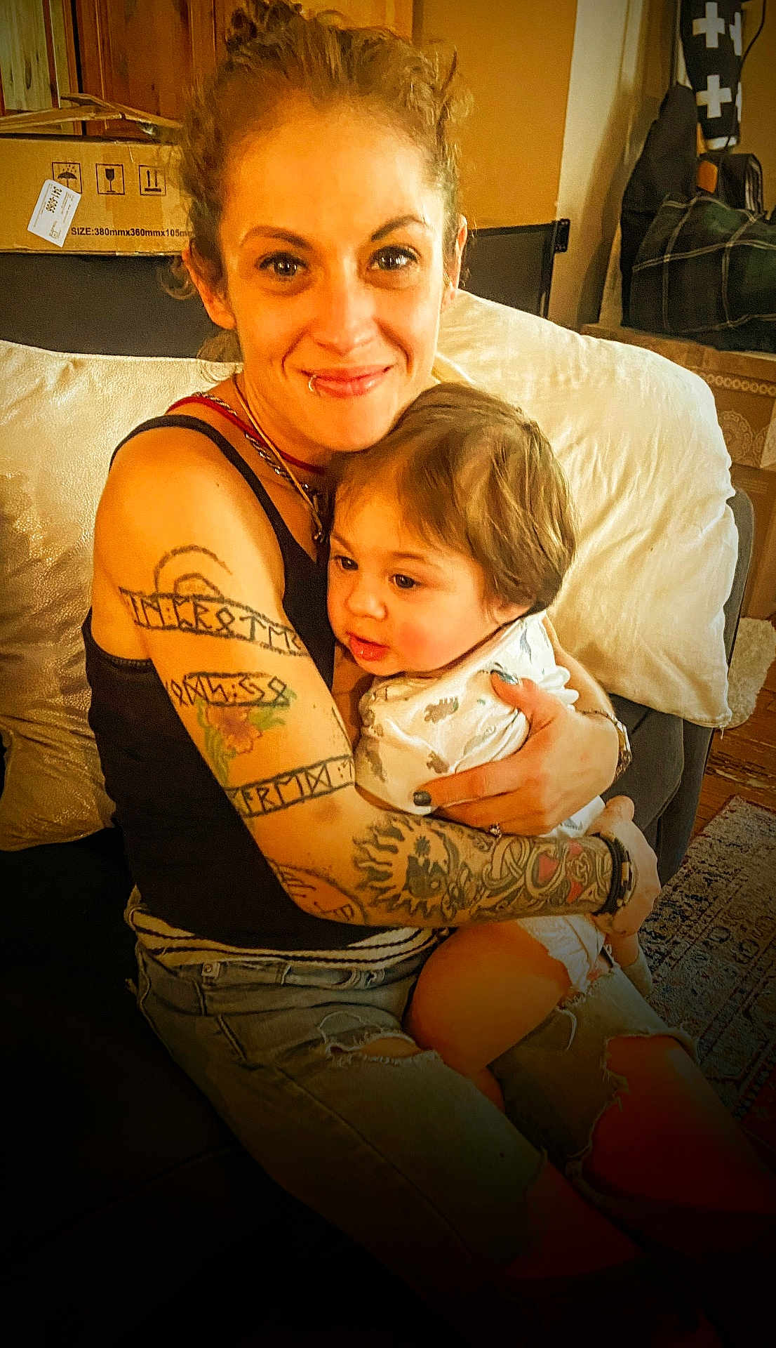 Micah joined the competition — help win amazing prizes! adult, baby, tattoo, hug, couch, home, people, smile, jeans, sitting, casual, indoor, comfort, child, affection, person, portrait, warmth, love, family