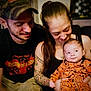 baby, baby_clothing, candid, cap, casual, closeup, facial_hair, family, happy, holding, indoor, intimate, love, man, people, portrait, pumpkin_pattern, smiling, tattoos, woman