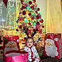 Milan is registered to the contest to win money with this photo: toddler, child, christmas_tree, holiday, pajamas, reindeer_antlers, gift_bags, decorations, ornaments, lights, indoors, carpet, festive, celebration, smiling, sitting, cute, christmas, happy, winter