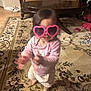 toddler, child, pink_sunglasses, heart_shaped, indoor, carpet, living_room, furniture, sofa, table, barefoot, motion_blur, cute, playful, clothing, toy, floor, headwear, person, young_child