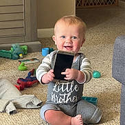 Weston James Howell is registered to the contest to win money with this photo: baby, brother, carpet, child, clothing, cute, face, floor, furniture, happy, holding, home, indoor, infant, person, play, sitting, smartphone, smiling, toys