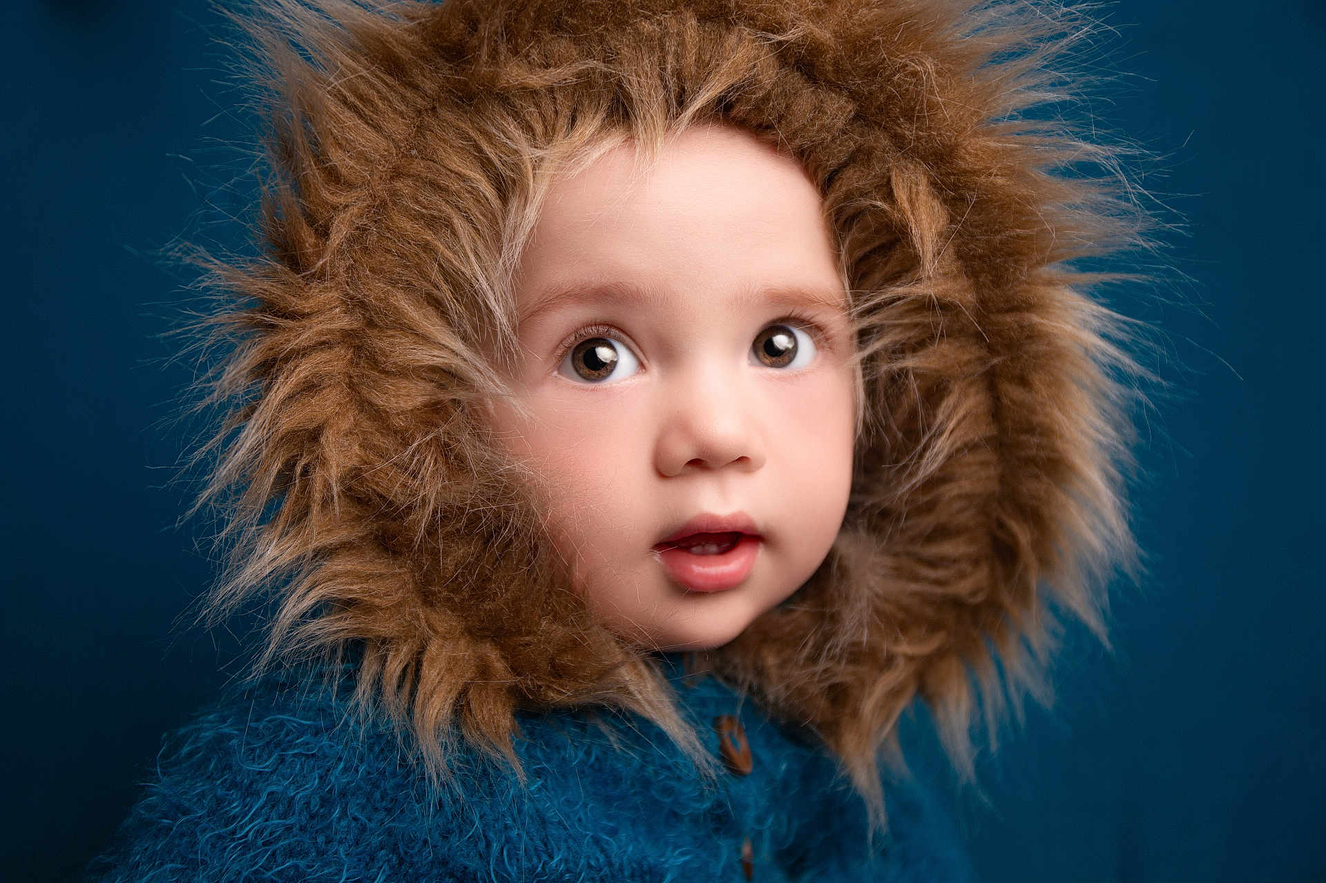 Oliver is registered to the contest to win money with this photo: child, toddler, face, fur_hood, blue_sweater, portrait, curious, wide_eyes, cozy, warm_clothing, studio, closeup, cute, baby, winter_wear, expression, headwear, innocent, soft_texture, indoor