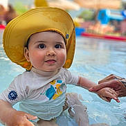 Yago a rejoint le concours — aidez-le/la à gagner de superbes lots ! baby, child, water, pool, hat, yellow_hat, swimwear, hand_holding, tattoo, outdoor, summer, cute, infant, sitting, water_play, sun_protection, skin, face, expression, daylight