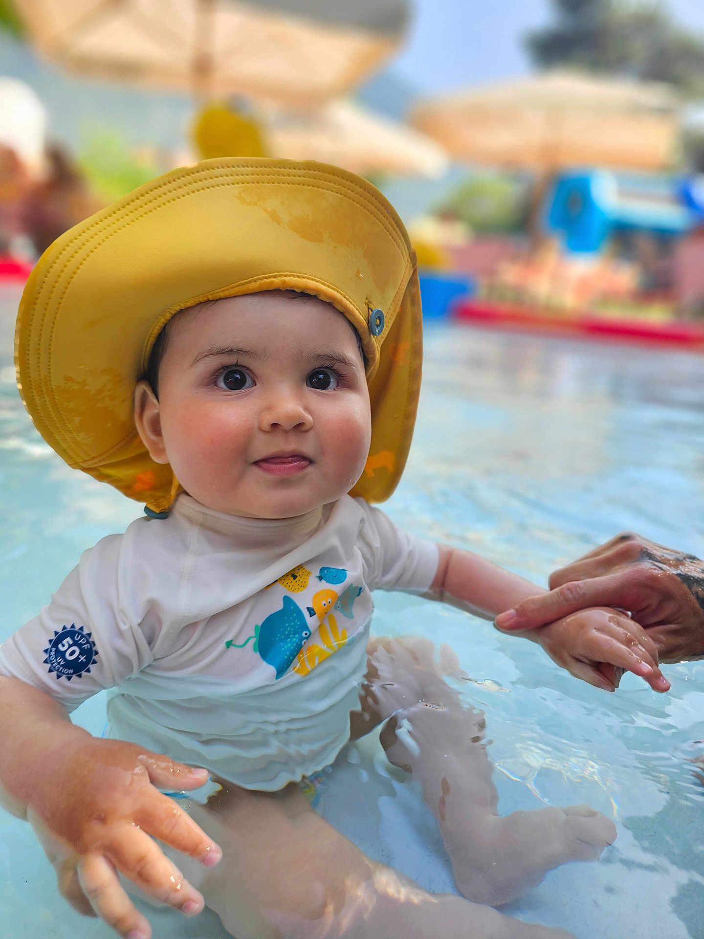 Yago a rejoint le concours — aidez-le/la à gagner de superbes lots ! baby, child, water, pool, hat, yellow_hat, swimwear, hand_holding, tattoo, outdoor, summer, cute, infant, sitting, water_play, sun_protection, skin, face, expression, daylight