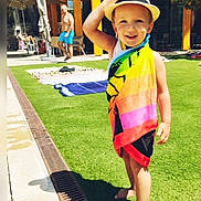 Hadj a rejoint le concours — aidez-le/la à gagner de superbes lots ! child, towel, hat, barefoot, smiling, outdoor, grass, poolside, sunny, building, umbrella, adult, summer, vacation, recreation, person, leisure, daytime, happy, casual
