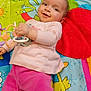 baby, child, smiling, toy, play_mat, colorful, clothing, pink_pants, long_sleeve_shirt, face, hand, floor, indoor, cute, infant, happy, pattern, cartoon, animal, flower