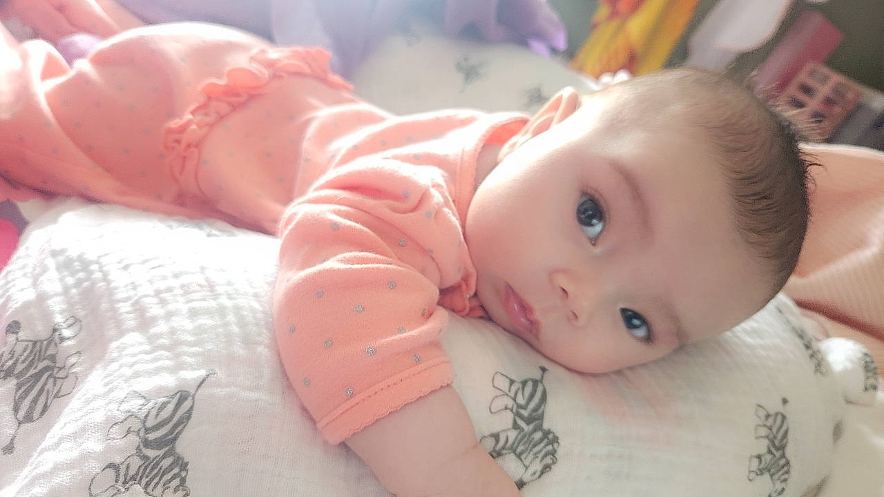 Ava is registered to the contest to win money with this photo: arm, baby, baby_toddler_clothing, cheek, chin, eye, eyebrow, eyelash, facial_expression, finger, hand, human_body, iris, lip, mouth, nose, person, pink, skin, sleeve