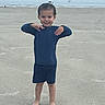 child, beach, sand, ocean, waves, water, barefoot, smiling, pose, blue_clothing, boy, young, outdoor, daytime, playful, shore, nature, happy, sea_bird, coast