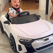 Joaquin is registered to the contest to win money with this photo: baby, child, toy_car, indoor, smiling, happy, floor, fireplace, christmas_stockings, pumpkin, living_room, seatbelt, white_car, audi, head, person, small_vehicle, tile_floor, furniture, holiday_decor