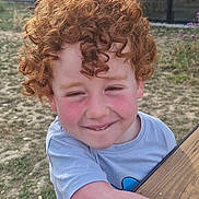 Maxen a rejoint le concours — aidez-le/la à gagner de superbes lots ! child, curly_hair, red_hair, smile, rosy_cheeks, outdoor, grass, wooden_table, tshirt, happy, face, person, nature, sunlight, freckles, cute, playful, young, boy, casual