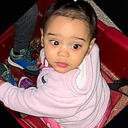 Malani is registered to the contest to win money with this photo: toddler, child, pink_jacket, pony_tail, red_wagon, sneakers, curious, looking_sideways, pants, cozy_clothing, outdoor, play, young_child, person, casual_clothing, footwear, seat, toy, expression, jacket