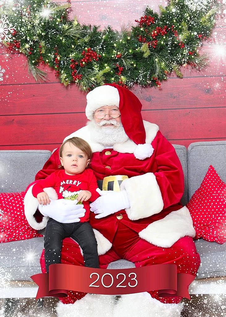 Elijah is registered to the contest to win money with this photo: baby, beard, christmas, christmas_eve, event, fictional_character, grass, happy, hat, headwear, holiday, human_body, lap, person, plant, red, santa_claus, sitting, smile, toddler