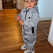 Lucas a rejoint le concours — aidez-le/la à gagner de superbes lots ! toddler, child, curly_hair, headband, nike, tracksuit, grey_clothing, sneakers, adidas, wooden_floor, indoor, person, standing, holding_object, bathroom, door, casual, home, flooring, portrait