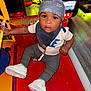 toddler, child, arcade, game, bandana, white_sneakers, red_surface, indoor, toy, play, curious, person, clothing, pants, shirt, pacifier, floor, light, colorful, hand