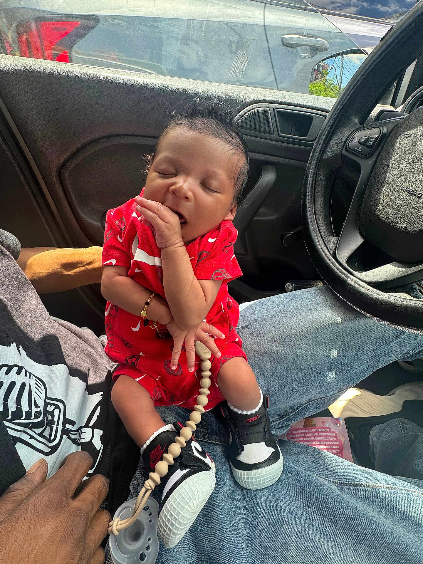 Chōzyn is registered to the contest to win money with this photo: baby, infant, child, person, sitting, car_interior, steering_wheel, clothing, sneakers, nike, pacifier, red_outfit, hand, jeans, sleeping, cute, indoor, window, sunlight, bracelet