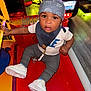 toddler, child, arcade, game_machine, bandana, white_sneakers, red_surface, curious, indoor, flooring, pacifier, bracelet, clothing, short_sleeve, pants, toy, play, entertainment, colorful, person