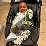 baby, smiling, sneakers, stroller, blanket, floor, tile, clothing, infant, footwear, person, indoor, happy, cute, child, sitting, portrait, head, face, playful