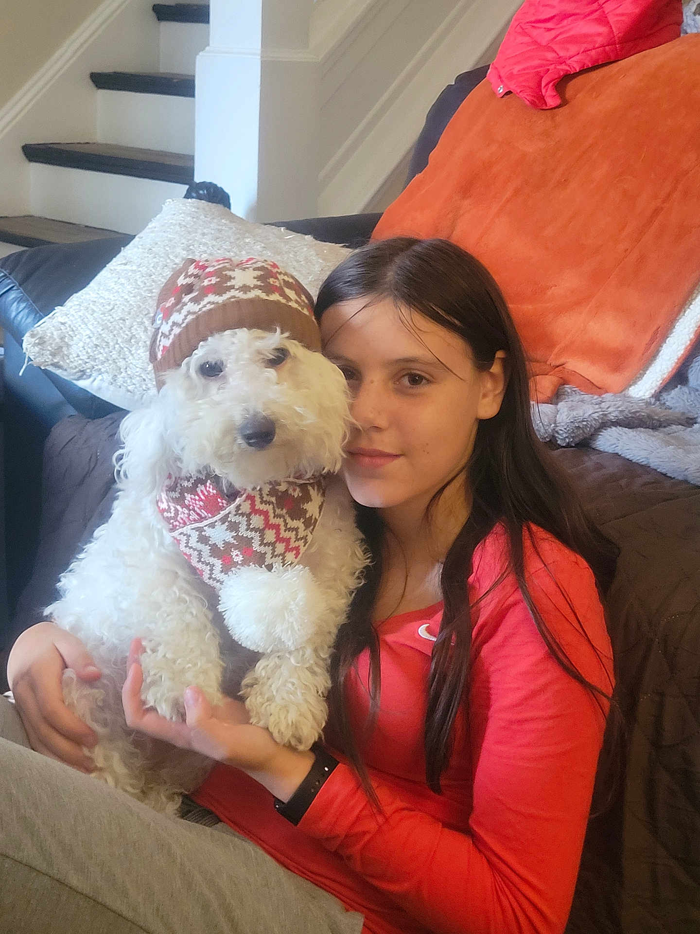 Jeter is registered to the contest to win money with this photo: girl, dog, white_dog, hat, scarf, indoor, living_room, couch, stairs, cushion, red_shirt, long_hair, pet, smiling, holding, cute, cozy, portrait, home, warm