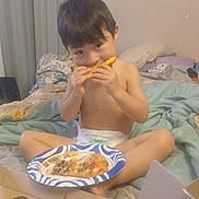 Misael is registered to the contest to win money with this photo: child, pizza, plate, bed, blanket, food, eating, indoors, casual, young_child, messy_bed, cardboard_box, person, snack, diaper, brown_hair, home, relaxed, meal, sitting