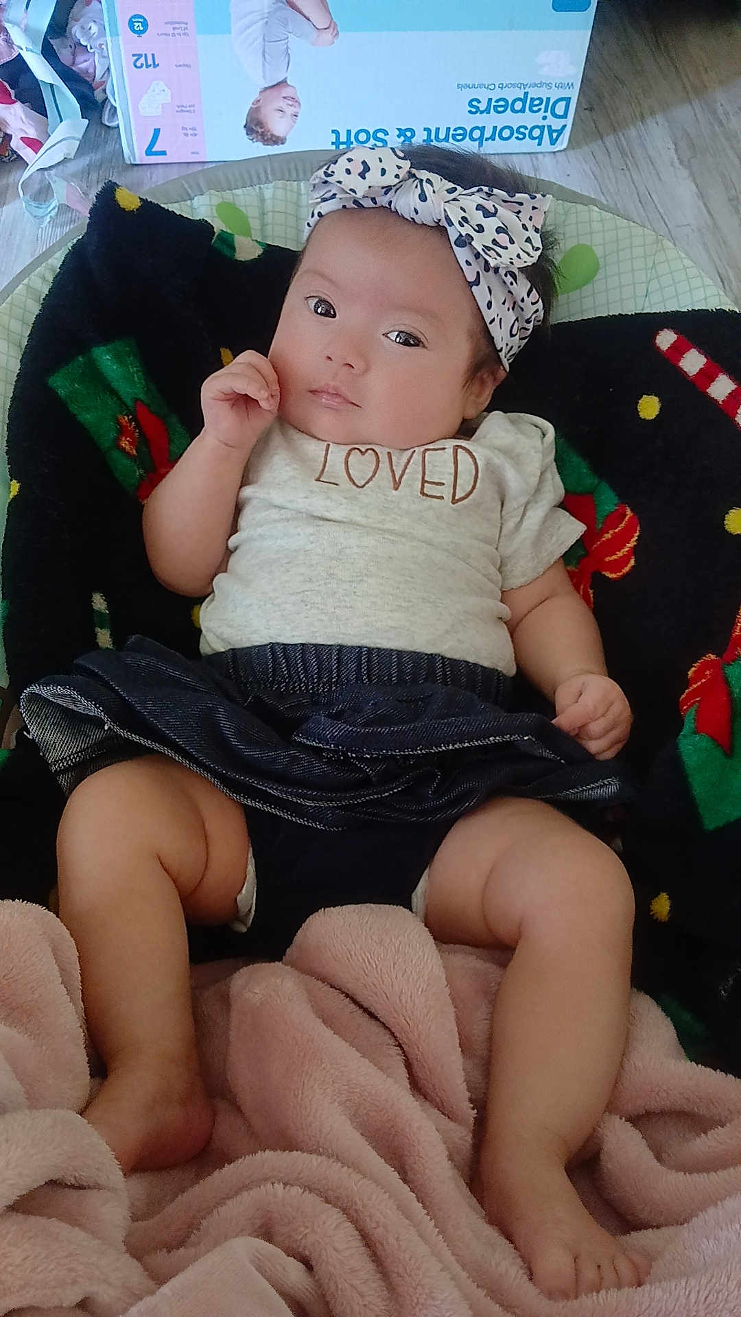 Mireya is registered to the contest to win money with this photo: baby, infant, headband, bow, shirt, diapers, blanket, floor, clothing, cute, child, person, indoor, soft_texture, pink, black, wooden_floor, relaxed, expression, portrait