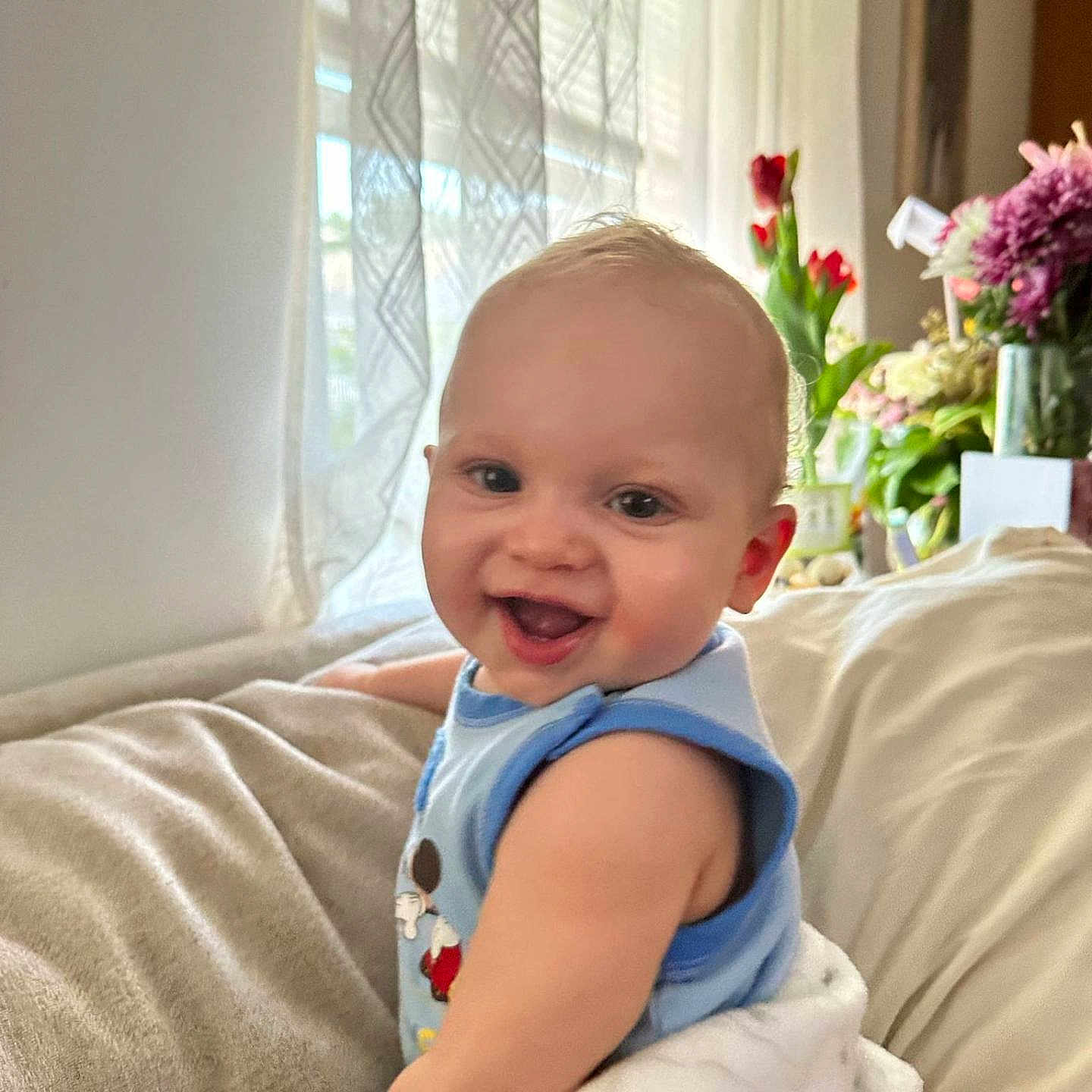 Messiah is registered to the contest to win money with this photo: baby, blanket, blue_clothing, child, couch, cozy, curtains, face, flowers, happy, home, indoor, infant, natural_light, person, portrait, smiling, soft_lighting, toddler, window