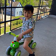 Anthony joined the competition — help win amazing prizes! child, toddler, tricycle, toy, green, outdoor, balcony, smiling, shorts, shirt, black_shoes, daylight, trees, railing, concrete_floor, play, person, cute, happy, vehicle