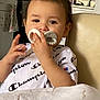 Arlo is registered to the contest to win money with this photo: toddler, child, pacifier, white_shirt, champion, indoor, kitchen, chair, person, baby, face, hand, expression, furniture, home, curious, seated, casual, young_child, comfort
