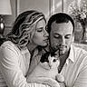 cat, couple, people, portrait, black_and_white, indoor, home, cuddling, embrace, pet, domestic_cat, white_shirt, woman, man, facial_expression, soft_lighting, window_light, furniture, cozy, photography