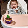 baby, child, high_chair, smile, cupcake, candle, number_8, birthday, chocolate, tray, harness, shirt, seat, happy, indoors, tile_floor, feeding_chair, portrait, celebration, cute