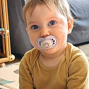 Joy participe au concours pour gagner de l'argent avec cette photo : baby, blond_hair, blue_eyes, child, closeup, cute, ear, face, gaze, hand, indoor, infant, onesie, pacifier, playmat, portrait, smile, sofa, soft_lighting, toddler