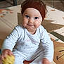 baby, infant, child, headband, blue_eyes, onesie, play_mat, toy_ball, sitting, smile, chubby_cheeks, indoor, tiled_floor, portrait, cute, brown_hair, hands, floor_mat, soft_lighting, closeup