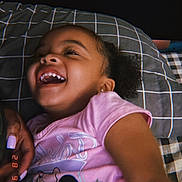 Nuri is registered to the contest to win money with this photo: child, girl, laughing, smiling, pink_shirt, minnie_mouse, pillow, checkered_pattern, curly_hair, earrings, bed, hand, nail_polish, close_up, indoor, happy, joy, portrait, family, candid