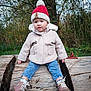 toddler, child, outdoor, winter_clothing, hat, pom_pom_hat, coat, jeans, boots, log, tree, forest, nature, grass, face, person, sitting, curious, cute, cold_weather