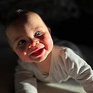 Ezio participe au concours pour gagner de l'argent avec cette photo : baby, infant, smiling, blue_eyes, face, closeup, portrait, crawling, onesie, hand, sunlight, shadow, soft_texture, blanket, cozy, cheeks, adorable, expression, indoor, bokeh