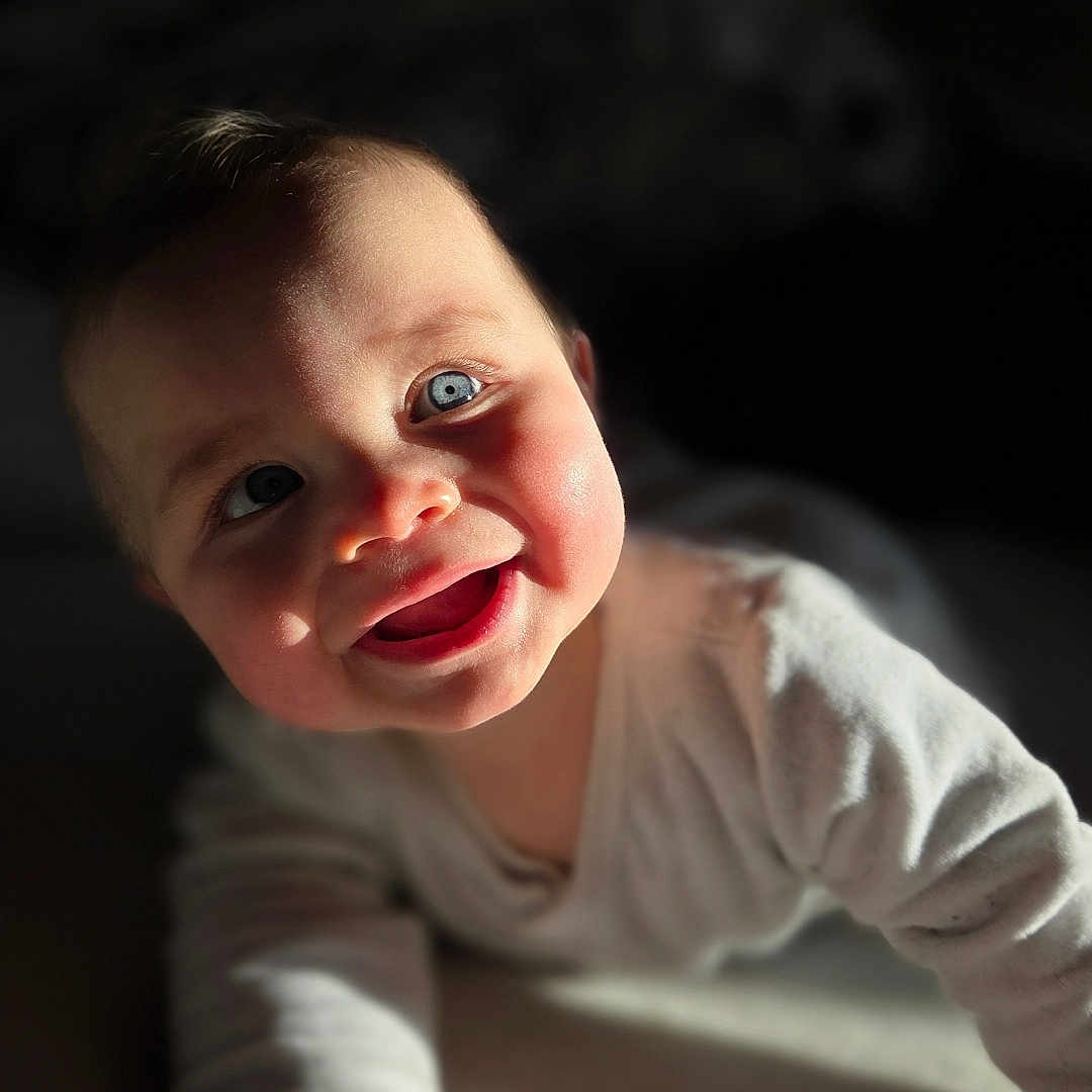 Ezio participe au concours pour gagner de l'argent avec cette photo : adorable, baby, blanket, blue_eyes, bokeh, cheeks, closeup, cozy, crawling, expression, face, hand, indoor, infant, onesie, portrait, shadow, smiling, soft_texture, sunlight