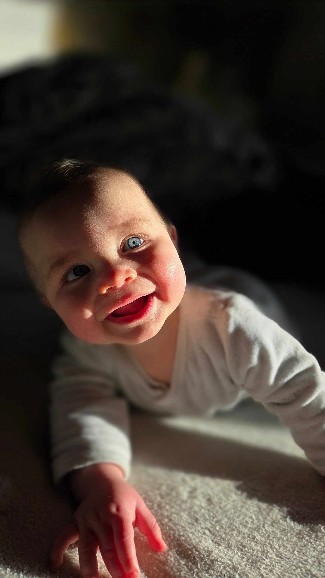 Ezio participe au concours pour gagner de l'argent avec cette photo : baby, infant, smiling, blue_eyes, face, closeup, portrait, crawling, onesie, hand, sunlight, shadow, soft_texture, blanket, cozy, cheeks, adorable, expression, indoor, bokeh