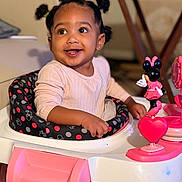 Nevaeh is registered to the contest to win money with this photo: toddler, child, baby_walker, toy, minnie_mouse, pink, smiling, indoor, person, happy, hair_puffs, seat, clothing, cute, playful, young_child, table, furniture, face, portrait
