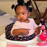 Nevaeh is registered to the contest to win money with this photo: toddler, baby_walker, child, toy, minnie_mouse, pink, curly_hair, pigtails, indoors, table, furniture, clothing, person, cute, expression, looking_away, seat, playful, young_child, home