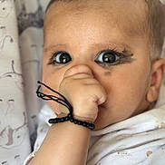 Baby is registered to the contest to win money with this photo: baby, infant, face, eyes, eyelashes, hand, thumb_sucking, bracelet, black_beads, smudged_makeup, closeup, portrait, blanket, curtain, clothing, skin, curious, cute, bokeh, indoors