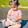 bow, casual, child, container, curious, cute, daylight, focused, grass, kneeling, outdoor, person, pink_clothing, playground, short_hair, sitting, sunlight, toddler, yellow_bar, young_child